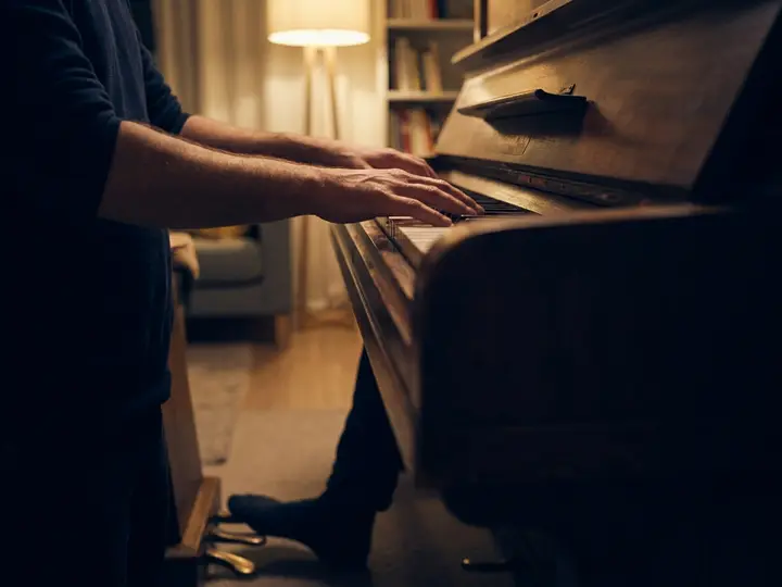 Fingers playing an arpeggio across the keys while a foot rests on the sustain pedal.